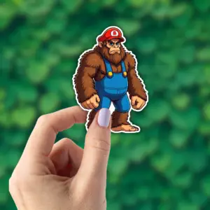 Hand holding a sticker of Bigfoot that looks like Mario.