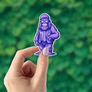 A hand holding a hipster Bigfoot sticker