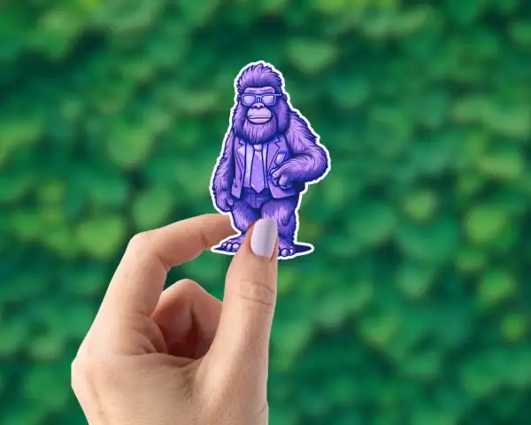 A hand holding a hipster Bigfoot sticker